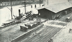 Ein Frachtschiff liegt am Kaiserkai des Hamburger Sandtorhafens - Pferdewagen mit Plane abgedeckt - Eisenbahnschienen und Waggons vor dem Lagerschuppen. ( ca. 1875 )