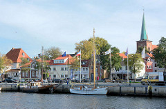 Blick über den Hafen von Neustadt in Holstein - Segelschiffe an der Hafenkante / Kai; Kirchturm der im 14. Jahrhundert erbauten Stadtkirche.