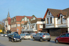 Unterschiedliche Architekturformen, Einzelhäuser mit Geschäften - Kieler Strasse in Quickborn; im Hintergrund der Kirchturm der Marienkirche.