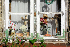 Altes Holzfenster mit Eisenwinkeln, abgeblätterte Farbe - Figuren als Fensterdekoration; Bilder aus Neustadt in Holstein.