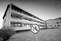 Dreistöckige Wohnanlage mit gelber Klinkerfassade, durchgehende Balkons mit Holzfassade - Schild Hunde verboten.