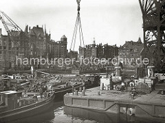 Im Sandtorhafen wird eine Lokomotive mit einem Schwimmkran aus dem Hafenbecken geborgen. Im Hintergrund die teilweise zerstörte Speicherstadt - an der Fassade des Verwaltungsgebäude der HHLA  ist ein Baugerüst zu erkennen. (1948)