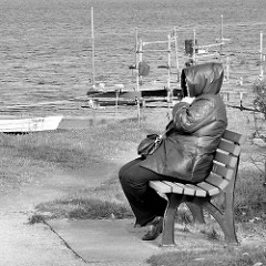 Ufer des Neustädter Binnenwassers - windiger, kühler Morgen, Frau mit dickem Mantel sitzt auf einer Bank am Wasser; Ruderboote, Fischerboote am Ufer des Sees.