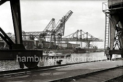 Blick über das Hafenbecken des Harburger Seehafens; im Vordergrund die Räder auf denen die Halbportalkräne auf der Kaimauer entlang geführt werden. Auf der gegenüber liegenden Seite des Hafenbeckens hat eine Schute festgemacht. (ca. 1938)