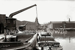 Binnenschiffe und Schuten haben an den Kais im Harburger Hafen festgemacht. Die Schiffer des Binnenschiffs GRETEL manövrieren ihr Schiff mit einem Bootshaken längsseits des Elbkahns. Ein Rollkran steht am Kai. (ca. 1938)