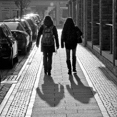 Gegenlichtaufnahme in Schwarz-Weiss; Fussgängerinnen mit langem Schatten, parkende Autos in der Bahnhofstrasse von Quickborn.