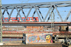 Eisenbahnbrücke über den Oberhafenkanal - ein S-Bahnzug fährt Richtung Veddel; im Hintergrund Speichergebäude am Billehafen in Hamburg Rothenburgsort / Grafitti mit gestrecktem Mittelfinger: Welcome in Hamburg.