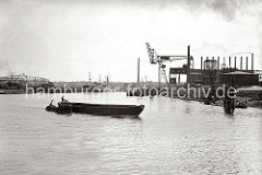 Eine Schute wird von der Barkasse HERTA aus dem Harburger Seehafen 3 auf die Süderelbe geschleppt; der Ewerführer steht auf dem Heck seines Lastkahns. Ein Seeschiff und ein Frachtsegler liegen an den Dalben des Hafenbeckens. (ca. 1938)