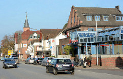 Unterschiedliche Architekturformen, Einzelhäuser mit Geschäften - Kieler Strasse in Quickborn; im Hintergrund der Kirchturm der Marienkirche.
