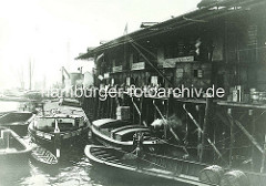 Schuppen der Vereinigten Elbschiffahrts-Gesellschaft im Magdeburger Hafen, Hafenbecken im Hamburger Hafen. Elbkähne liegen an der Kaianlage - ein Kran hebt eine Kiste, im Vordergrund ein Ewerführer mit Peekhaken auf seiner Schute - zwei Fässe