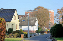Einzelhäuser mit Spitzdach; Vorgarten an einer schmalen Nebenstrasse, mehrstöckiger Wohnblock im Hintergrund. Bilder aus Quickborn, Kreis Pinneberg.