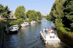 Ein Sportboot kommt aus der Schleuse am Baalensee und fährt in die Schleusenhavel in Fürstenberg ein. Weitere Motorboote warten am Ufer auf die Schleusung.