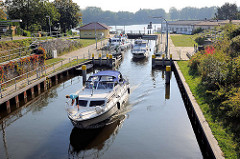 Ein Sportboot kommt aus der Schleuse am Baalensee und fährt in die Schleusenhavel in Fürstenberg ein; weitere Motorboote liegen noch in der Schleusenkammer.