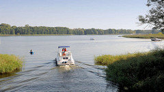 Ein Motorboot fährt auf der Havel in den Schwedtsee ein; re. im Hintergrund die Mahn- und Gedenkstätte Ravensbrück am Seeufer.