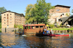 Ein Hausboot und Kanu auf der Havel an der Steinhavelschleuse - am Ufer die unter Denkmalschutz stehenden Gebäude der historischen Steinmühle.