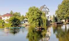 Kanus auf der Gänsehavel in Fürstenberg - Wohnhäuser und Bäume in der Sonne am Flussufer.