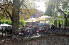 Restaurant / Café im Freien am Fischmarkt von Lüneburg - Gäste sitzen unter Sonnenschirmen an der Ilmenau.