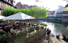 Restaurant / Café im Freien am Fischmarkt von Lüneburg - Gäste sitzen unter Sonnenschirmen an der Ilmenau.