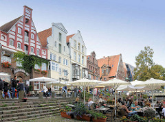 Aussengastronomie am Stintmarkt an der Ilmenau in der Hansestadt Lüneburg. Gäste sitzen unter Sonnenschirmen an der Ilmenau.