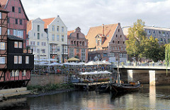 Aussengastronomie am Stintmarkt an der Ilmenau in der Hansestadt Lüneburg - zwei historische Boote, darunter ein sogenannter Salzewer liegen im Hafenbereich.