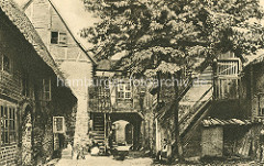 Alter Hinterhof - historische Architektur von Lüneburg; eine Frau sitzt in der Sonne auf der Holztreppe / Mann mit Pfeife - Roter Hahn ca. 1900.