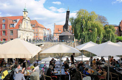 Restaurant unter Sonnenschirmen am Hafen von Lüneburg - im Hintergrund die Barockfassade vom Alten Kaufhaus und der Alte Kran am Hafenkai.