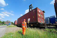 Beladen eines Containerzugs in Hamburg Wilhelmsburg - der Schwerlaststabler senkt den Container auf den Flachwagen - die Stahlbox rastet in den Halterungen ein; der Mitarbeiter dirigiert den Staplerfahrer in die richtige Position..