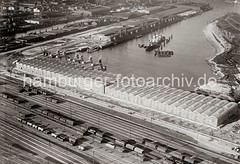 Luftfoto vom Windhukkai des Süd-West-Hafens,  dem Lagerschuppen 59  mit den Tonnengewölben am Veddeler Damm und den Gleisanlagen des Güterbahnhofs Hamburg Süd. Ein Frachter liegt an den Dalben in der Mitte des Hafenbeckens.