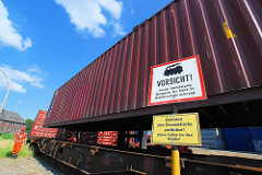Der Container wird auf den Güterwaggon abgesenkt - Schild Vorsicht privater Bahnübergang.