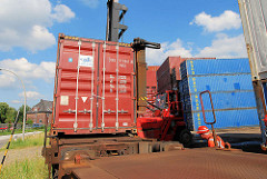 Beladen eines Containerzugs in Hamburg Wilhelmsburg - der Schwerlaststabler senkt den Container auf den Flachwagen - die Stahlbox rastet in den Halterungen ein; der Mitarbeiter dirigiert den Staplerfahrer.