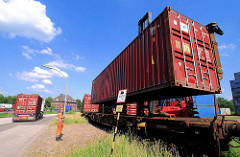 Beladen eines Containerzugs in Hamburg Wilhelmsburg - der Schwerlaststabler senkt den Container auf den Flachwagen - die Stahlbox rastet in den Halterungen ein; der Mitarbeiter dirigiert den Staplerfahrer in die richtige Position..