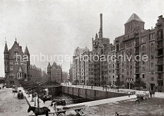 Auf der St. Annenbrücke fahren Pferdefuhrwerke; eines ist mit Säcken beladen; re. die Blöcke Q + R am St. Annenufer, eine Hieve Säcke wird gerade vom Speicherboden auf ein Fuhrwerk herunter gelassen.