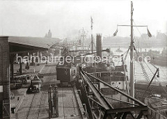 Blick auf hinteren Abschnitt des Baakenhafen mit dem Schuppen 25 am Versmannkai. Ein Rollkran belädt einen Frachter mit Ballen - Kaiarbeiter bereiten auf der Laderampe den Transport weiterer Güter vor.