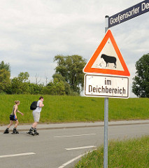 Schild Achtung Schafe im Deichbereich - Rollerskating auf der Deichstrasse am Goetjensorter Deich in Hamburg Wilhelmsburg.