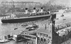 Das Passagierschiff Cap Arcona hat von den Landungsbrücken abgelegt und ist bereit zur Ausreise. Ein Schlepper befindet sich am Bug des Dampfers. Am gegenüber liegenden Elbufer die Werftanlagen mit Hellingen und Industriegebäuden.
