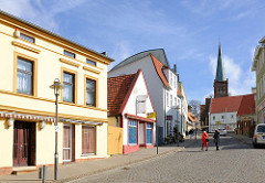 Unterschiedliche Architekturstile und farbig gestaltete Hausfassaden, Marktstrasse / Bahnhofstrasse in Bergen - im Hintergrund der Kirchturm der St. Marienkirche.