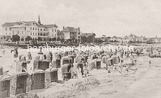 Altes Bild einer Strandszene am Binzer Ostseestrand auf Rügen - Holzboot / Ruderboot am Wasser; Strandkorb in der Sonne - im Hintergrund Häuser an der Strandpromenade.