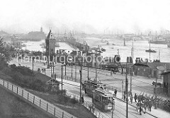 St. Pauli Landungsbrücken ca. 1900 - zwei Strassenbahnen an der Haltestelle Landungsbrücken; ein Arbeiter trägt mehrere Milchkannen, ein anderer transportiert ein Fass auf der Handkarre. Leere Karren sind an der Strasse abgestellt.