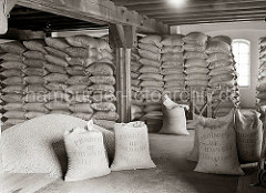 Der Kaffee aus Kolumbien ist in Jutesäcke vernäht und bis an die Decke des Speicherbodens gestapelt. Die Säcke tragen die Aufschrift Produkt of Colombia - 70 Kilos. Ein Haufen Kaffee ist auf dem Lagerboden ausgeschüttet.