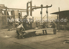 Eine Eisenplatte wird von den Werftarbeitern unter die Dampfschere gelegt. Schiffswerft und Maschinenfabrik Heinrich Brandenburg auf Hamburg Steinwerder.