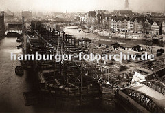der Bau der neuen Hamburger Speicherstadt hat begonnen - die Fleete sind ausgehoben und werden mit neu errichteten Brücken überspannt, Schuten transportieren das Baumaterial. Im Vordergrund wird der Speicherblock G gebaut.