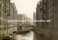 Schuten im Fleet in der Hamburger Speicherstadt - die Kähne sind mit Säcken beladen und an den Ringen, die in der Speichermauern eingelassen sind fest gemacht. Eine über dem Wasser hängende Lampe soll die Arbeiten in der Dunkelheit erleichtern.