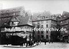 Strassenkreuzung im Bereich Pickhuben - die historischen Häuser stehen dicht gedrängt in dem zukünftigen Areal der Hamburger Speicherstadt. Ein Ladenschild links weist auf eine Barbier Stube hin sowie auf einen Klempner und Mechaniker.