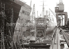 Schwimmdock der 1877 gegründeten Werft Blohm & Voss - Werftkräne stehen am Rand des Docks und transportieren Arbeitsmaterial zum Schiff. Im Vordergrund liegen ein Schwimmkran und eine Arbeitsschute.