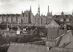 Blick über den Sandtorhafen zu den neogotischen Backsteinbauten der Hamburger Speicherstadt. Am Sandtorkai liegt ein Frachtschiff, dahinter die Hafenkräne vor dem Lagerschuppen 7.