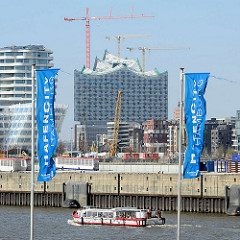 Flaggen der Hafencity Hamburg, eine Barkasse fährt am Chicagokai / Strandkai; Baukräne und Baustelle der Elbphilharmonie.