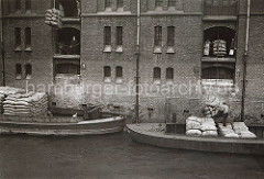 Warenumschlag in der Speicherstadt - die Ladung zweier Schuten wird gelöscht. Mit den Winden, die sich unter den Dächern der Speichergebäude befinden, werden die Säcke auf die Böden der Lagerräume gebracht.