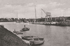 Historische Ansicht vom Hafen in Dömitz; zwei Lastkähne liegen am Ufer - weitere werden von einer Barkasse gezogen. Binnenschiffe liegen am Kai beim Hafenkran - Güterwaggons auf den Gleisen.