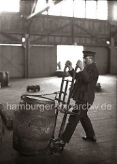 Bei einer Selbstladekarre wird das Fass beim Beladen mit einem eisernen Haken, der an einer Kette befestigt ist, auf die Handkarre gezogen. So kann der Lagerarbeiter die Tonne ohne grossen Kraftaufwand an ihren Bestimmungsort transportieren.