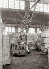 Mit einem fahrbaren Schuppenkran der Fa. Lauchhammer transportiert der Kranführer eine große Holzkiste im Schuppen. Zwei Lagerarbeiter dirigieren die Last an ihren Platz; ca 1934.